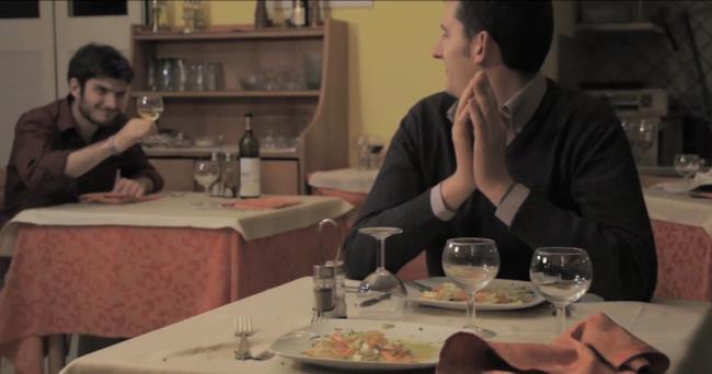 Anche per la Festa della Donna i Minimad rinnovano il consiglio di diventare froci Un uomo ammicca ad un altro e alza il calice di vino per salutarlo nel video dei Minimad