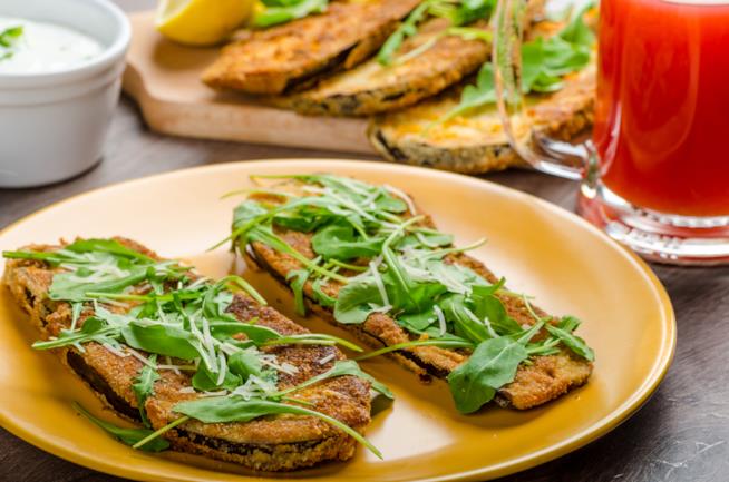 Hamburger di melanzane e provola affumicata: la ricetta Piatto piano con fondo giallo, all'interno 2 hamburger di melanzane con rucola