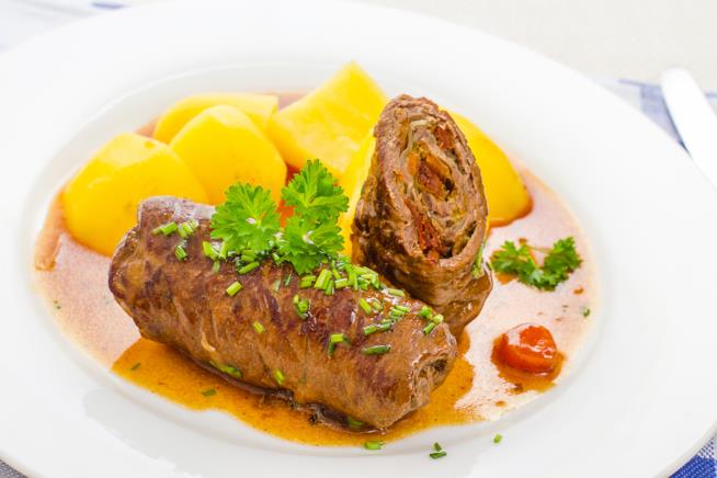 Braciole farcite con erbe aromatiche: la ricetta Piatto bianco con all'interno due braciole di carne di cui una intera e l'altra a metà con patate.