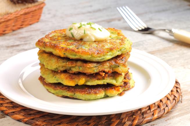 Ricetta tradizionale americana rivisitata in versione salata: ecco i pancakes con carote e zucchine Pancakes alle verdure su piatto bianco rettangolare