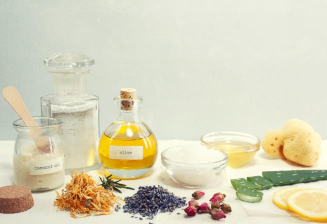 Cosmetica naturale: curare pelle e capelli con prodotti vegani Cinque flaconi contenenti olio e polveri, una spugna circondati da verdure e erbe naturali