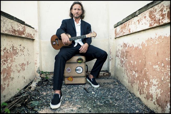 Il cantante Eddie Vedder Eddie Vedder con una chitarra in mano, seduto su una valigia, vestito di nero