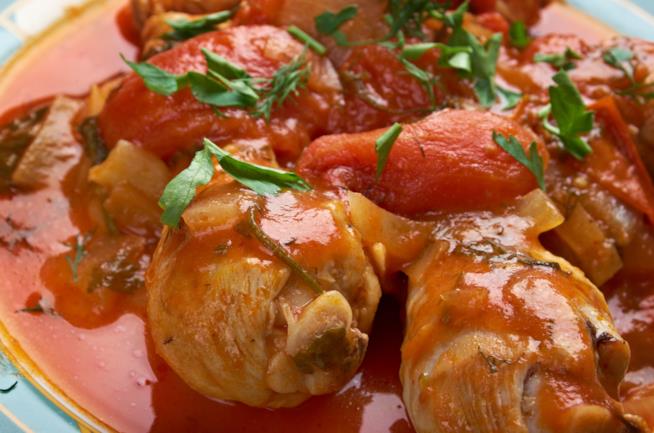 Pollo alla cacciatora: la ricetta Primo piano di pezzi di pollo con pomodori pelati e prezzemolo tritato