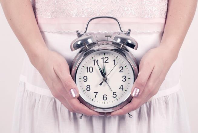Si può allontanare il momento della menopausa Donna regge una sveglia con entrambe le mani