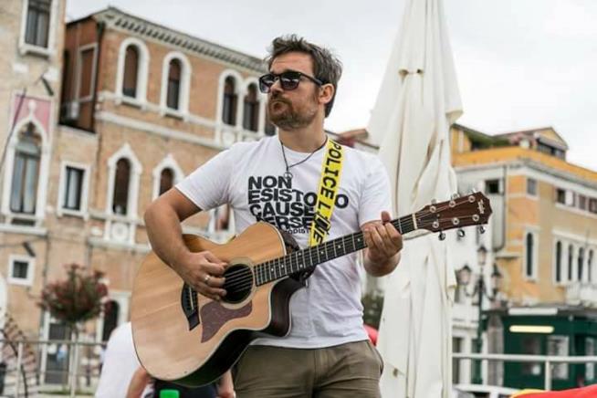 Via Emilia è il nuovo album di Jack Anselmi Jack Anselmi con una maglietta bianca, mentre suona la chitarra, con lo sfondo di Venezia
