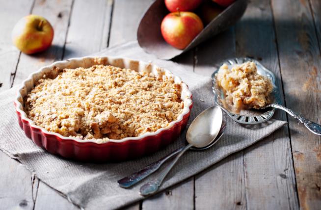 Crumble alle mele, un dolce tipico anglosassone a base di mele nella versione tradizionale Crumble di mele su tavolo di legno circondato da mele e cucchiai