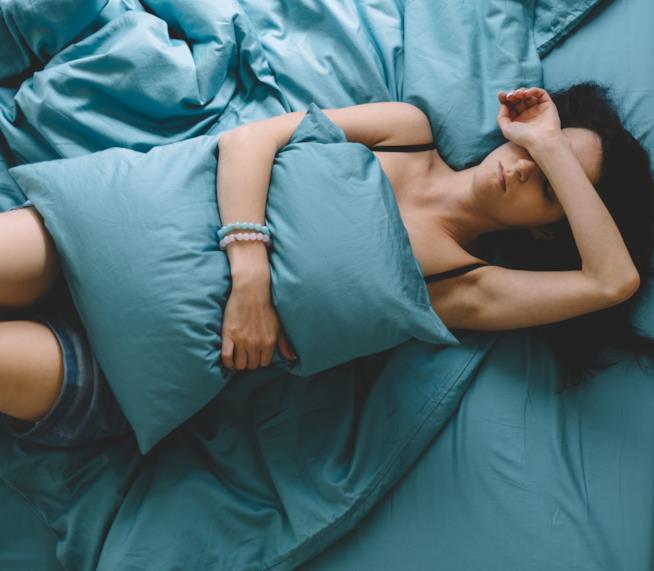 Rimedi naturali per i dolori del ciclo Una ragazza è sdraiata sul letto con un cuscino sulla pancia