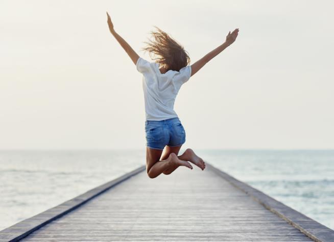 La vera felicità secondo i danesi Ragazza su un molo che salta per la felicità