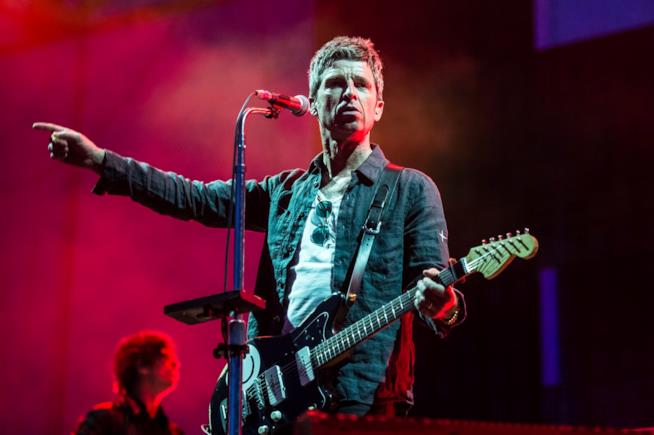 Noel Gallagher agli I-Days Noel Gallagher in piedi, con la chitarra in mano, di fronte a un microfono, con un braccio alzato