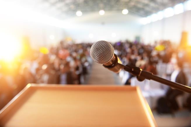 Una conferenza per le donne gestita da uomini Sala gremita di persone con un microfono in primo piano