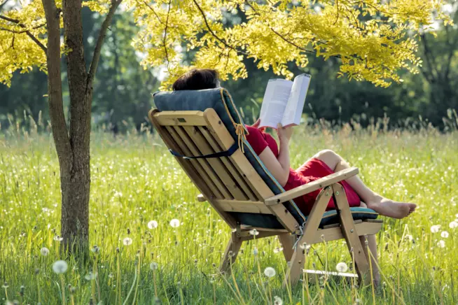 Nell'area relax all'aperto non può mancare un portariviste di design per avere sempre a portata di mano giornali e libri preferiti Ragazza che legge un libro seduta su una sdraio in giardino
