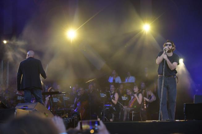 I Thegiornalisti in concerto Tommaso Paradiso, in piedi al microfono, davanti all'orchestra