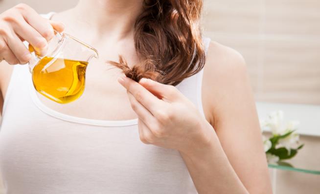 Come ristrutturare i capelli in modo naturale Una ragazza tiene tra le mani una ciocca di capelli e dell'olio