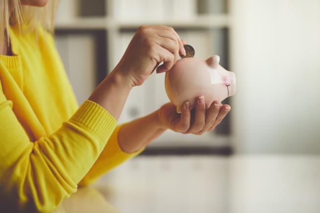 Risparmiare soldi si può: una lista di buone abitudini da fare proprie. Una donna che mette una moneta nel salvadanaio.