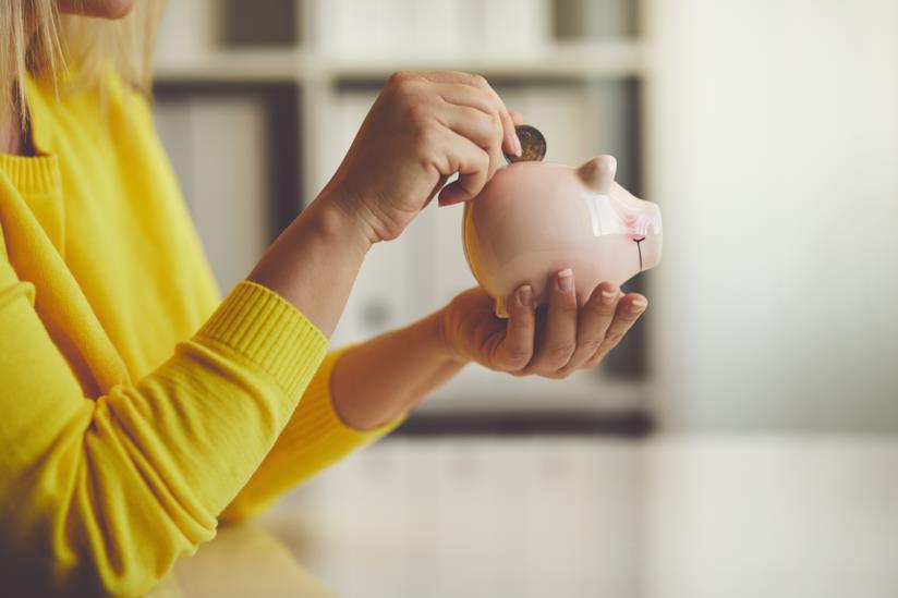Risparmiare soldi si può: una lista di buone abitudini da fare proprie. Una donna che mette una moneta nel salvadanaio.