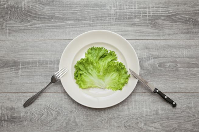 Un piatto, posate ed insalata Un piatto che contiene una foglia d'insalata