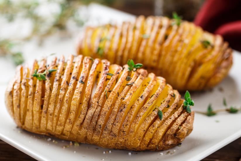 Patate hasselback per un contorno sfizioso e invitante secondo la tipica ricetta svedese Patate hasselback su piatto di ceramica bianco