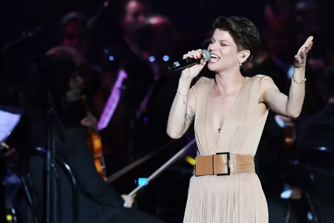 Alessandra Amoroso e i Tiromancino insieme Alessandra Amoroso canta, in piedi e con gli occhi chiusi, al microfono, vestita in marrone chiaro
