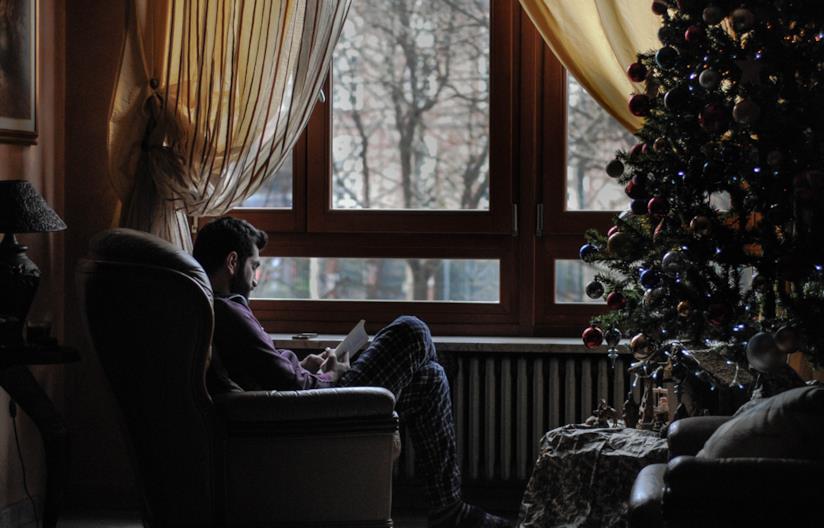 Una casa calda e accogliente è fatta di dettagli personali e colori piacevoli Persona seduta in poltrona accanto alla finestra e al radiatore in un pomeriggio d'inverno