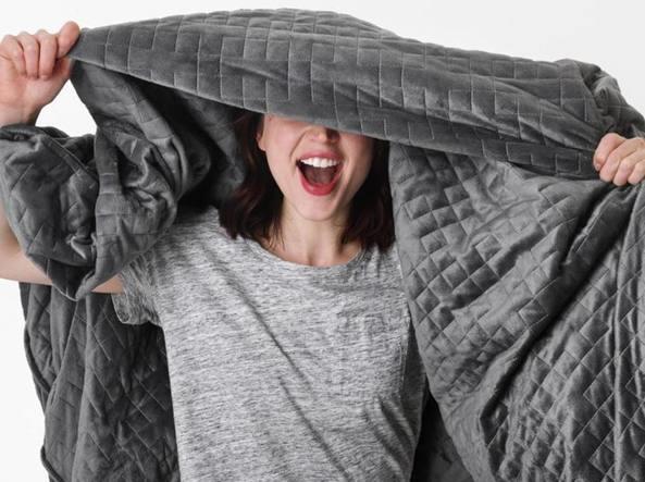 Gravity blanket è il nuovo oggetto per tutte le persone che soffrono di insonnia Una ragazza con una t-shirt grigia si copre con una gravity blanket