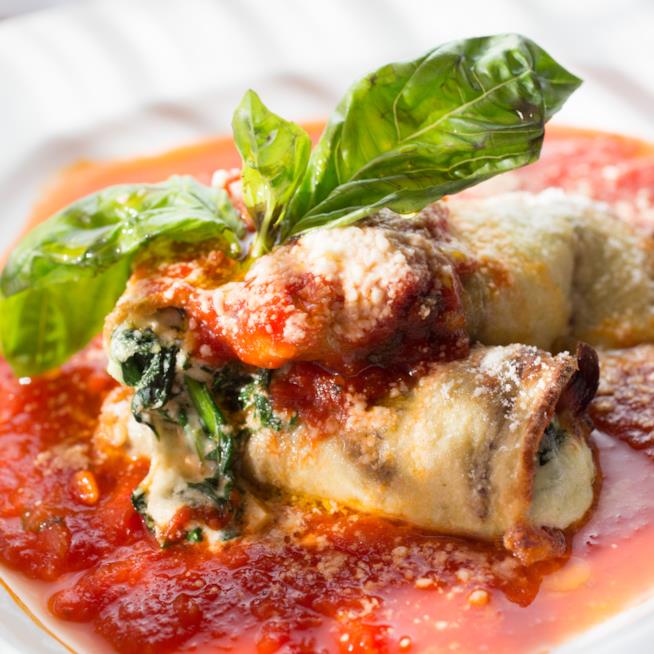 Involtini di melanzane ripieni: la ricetta Primo piano di involtini di melanzane ripieni con spinaci e fontina, ricoperti con salsa di pomodoro