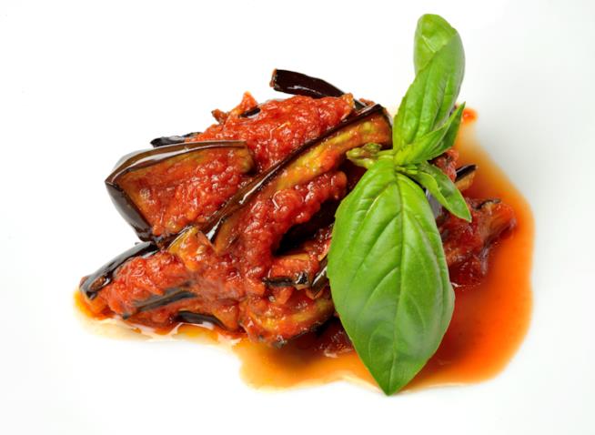 Melanzane a funghetto: la ricetta Primo piano di melanzane con passata di pomodoro e foglie di basilico fresco