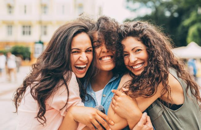 Benefici del sorriso Tre ragazze si abbracciano sorridendo