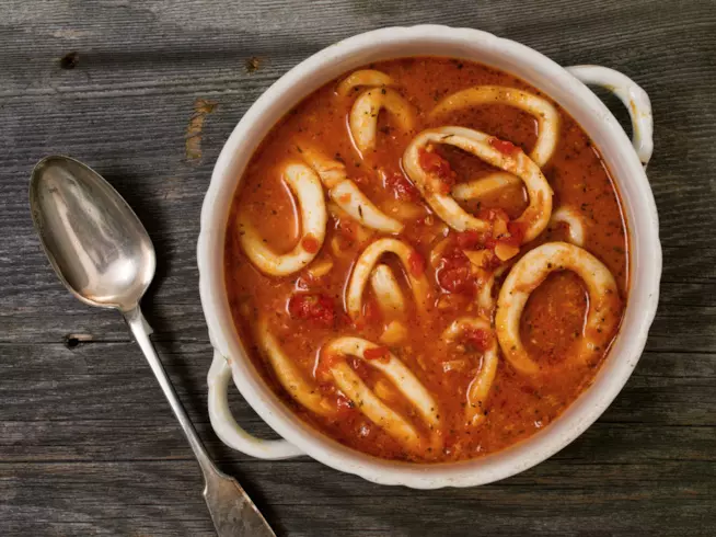 Calamari affogati: la ricetta Primo piano di calamari con salsa di pomodoro in un piatto di porcellana bianco
