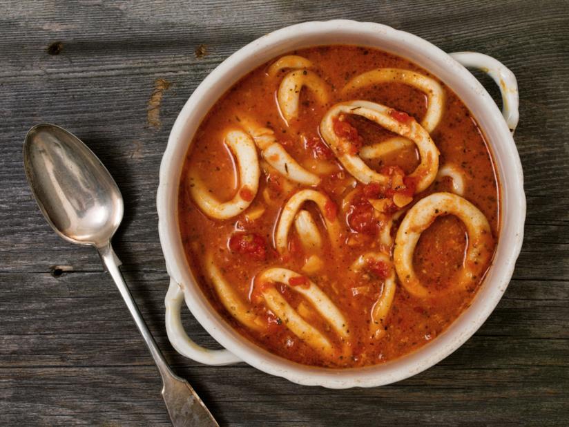 Calamari affogati: la ricetta Primo piano di calamari con salsa di pomodoro in un piatto di porcellana bianco