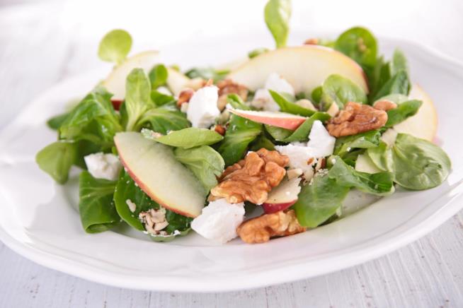 Insalata con songino, mele e scaglie di parmigiano: la ricetta Primo piano di songino, mele, noci e scaglie di parmigiano su piatto di ceramica bianca
