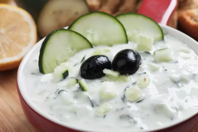 Ricetta tradizionale della salsa tzatziki, tipico condimento greco a base di yogurt greco, aglio e cetriolo Ciotola con salsa tzatziki guarnita con fettine di cetriolo e olive nere