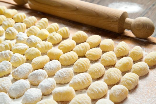 Gnocchi di patate da preparare in casa: la ricetta Tagliere di legno con gnocchi di patate cosparsi di farina e mattarello di legno in fondo
