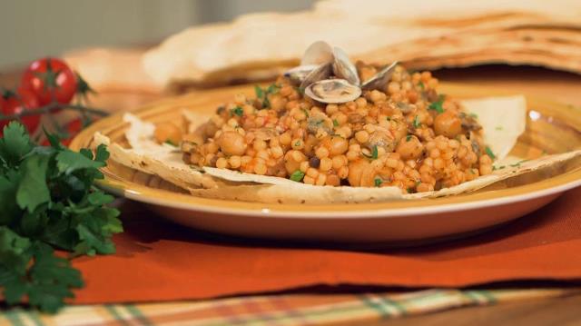 Fregola con vongole e ceci: la ricetta di Giallo Zafferano Primo piano di fregola sarda con vongole e ceci su piatto bianco