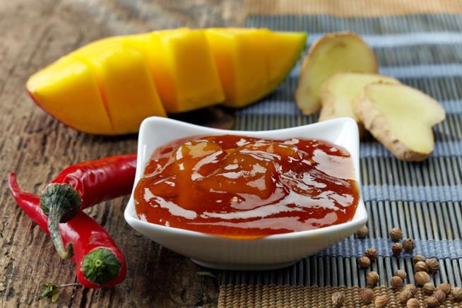 Chutney di mango e zenzero: la ricetta Ciotola bianca quadrata con chutnay di mango e zenzero, al lato due peperoncini rossi e pepe