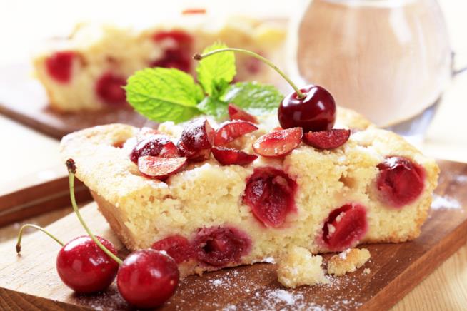 Torta morbida allo yogurt e ciliegie, una ricetta golosa e veloce da realizzare Quadrotto di torta allo yogurt e ciliegie con fogliolina di menta su tagliere di legno