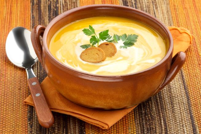Vellutata di carote e curry: la ricetta Primo piano di tegame in terra cotta con all'interno vellutata di carote, crostini e prezzemolo