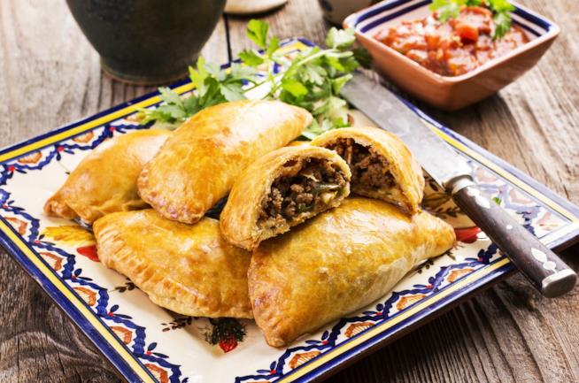 Empanadas argentine con carne: la ricetta Piatto di ceramica decorato ai bordi con all'interno delle empanadas di carne