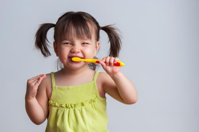 Giocare a lavarsi i denti Bimba che gioca con lo spazzolino da denti