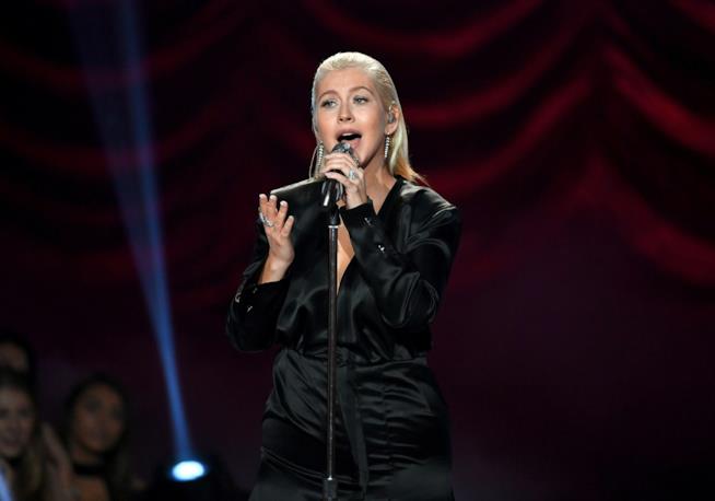 Twice è la nuova canzone di Christina Aguilera Christina Aguilera, in nero, su sfondo rosso, canta in piedi al microfono