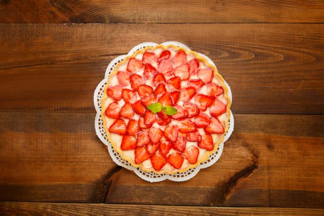 Torta di fragole e crema pasticcera: un tripudio di gusto e di colori Crostata di fragole e crema pasticcera adagiata su centrino bianco