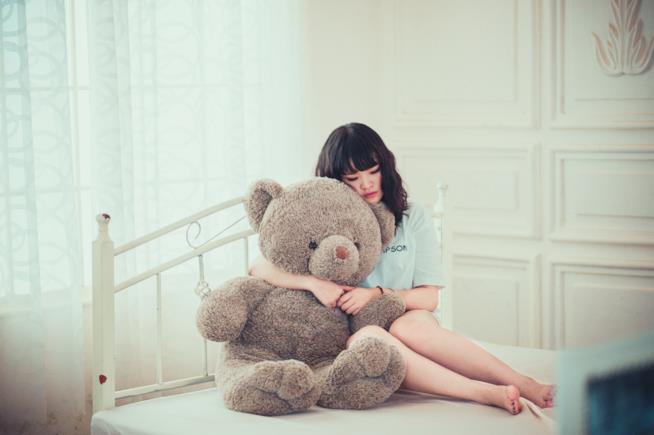 Depressione estiva Una ragazza abbraccia un pupazzo sul letto