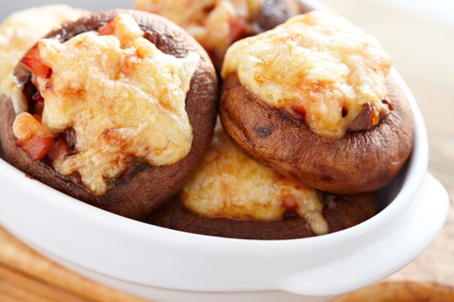 Funghi porcini farciti: la ricetta Primo piano di funghi porcini farciti con mozzarella e prosciutto su piatto bianco