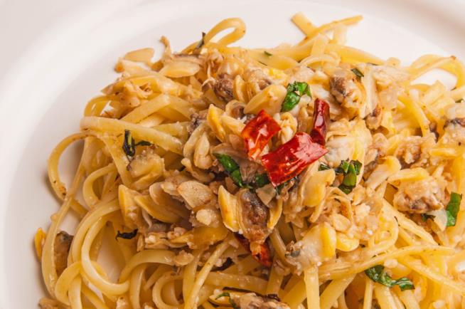 Linguine con vongole e taralli: la ricetta Primo piano su piatto bianco di linguine con vongole, taralli, peperoncino e prezzemolo