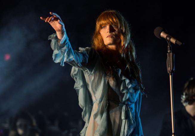 I Florence + The Machine a Torino a Bologna Florence Welch in piedi, davanti al microfono, con un vestito celeste e un braccio alzato