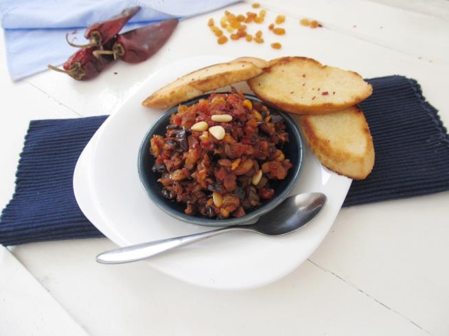 Caponata di melanzane con olive, capperi, uvetta, pinoli e servita con crostini di pane Caponata con melanzane fritte in salsa di pomodoro agrodolce