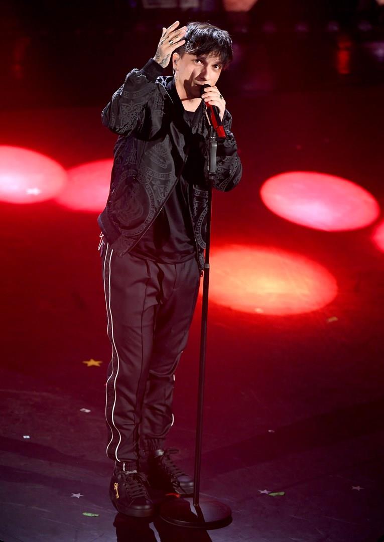 Il cantante Ultimo Ultimo, in piedi, vestito di nero, di fronte al microfono
