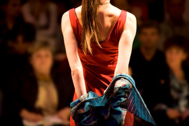 Abbigliamento cruelty free, l’alternativa vegan nel guardaroba. una ragazza con vestito rosso sfila vista da dietro mentre si leva una giaccia