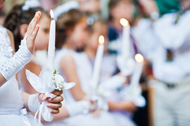 Frasi Cresima Bambina durante il rito della Cresima che tiene in mano una candela