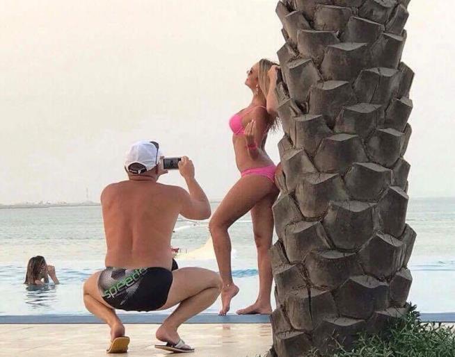un uomo fotografa una donna appoggiata ad una palma Un uomo scatta foto ad una donna in posa vicino ad una palma