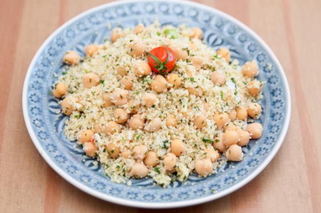 Cous cous con ceci: la ricetta Piatto di ceramica lavorata con blu e all'interno cous cous di ceci, erba cipollina e un pomodorino